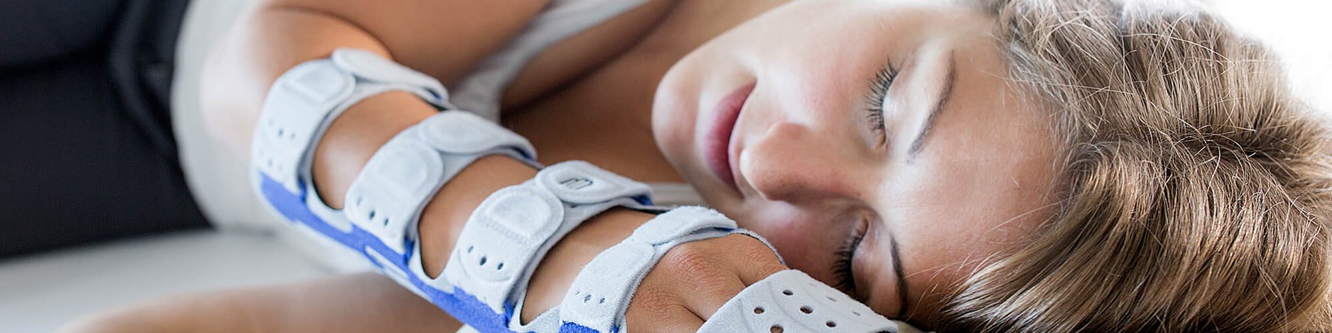 Eine Frau liegt auf der Seite auf einem weissen Kissen und schläft. Sie trägt eine ManuLoc long Plus am rechten Arm und an der Hand, die mit Klettverschlüssen befestigt ist.