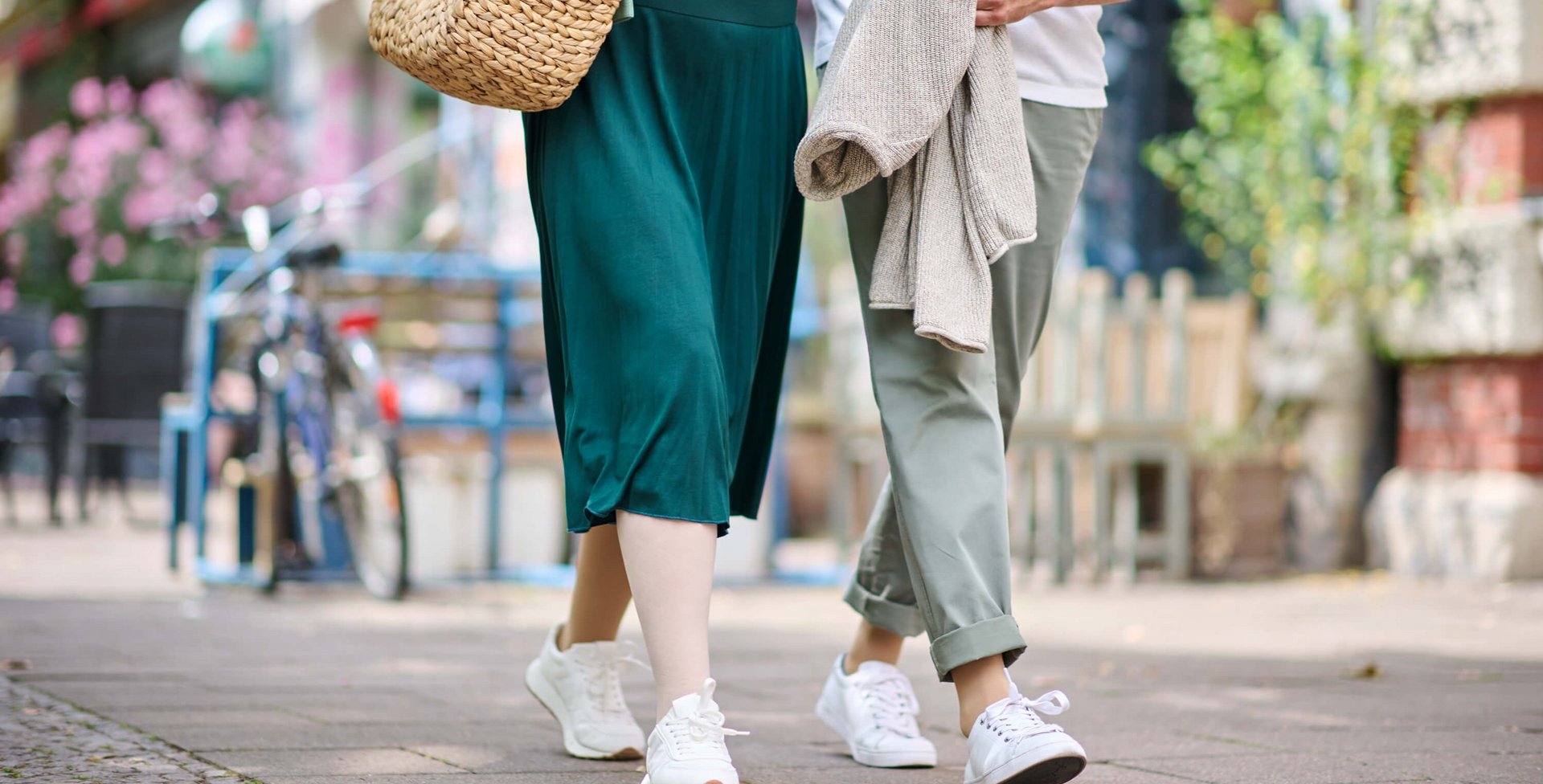 Ein Paar geht entspannt durch eine sommerliche Stadt. Beide tragen weiße Sneakers, und die Frau trägt wirksame Kompressionsstrümpfe aus der VenoTrain Special-Linie.