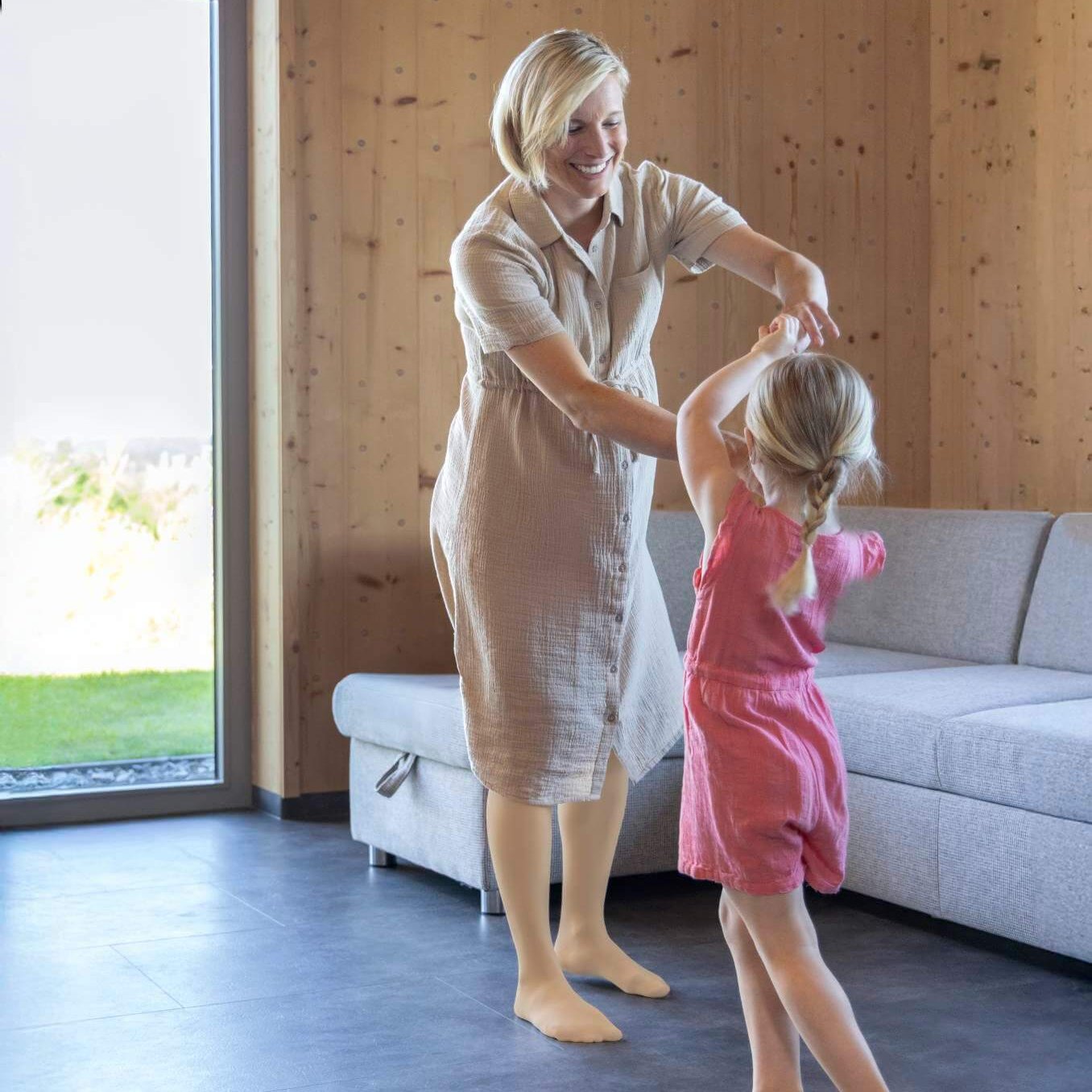 Schwangere Mutter und Tochter tanzen fröhlich barfuß im Wohnzimmer vor dem Sofa