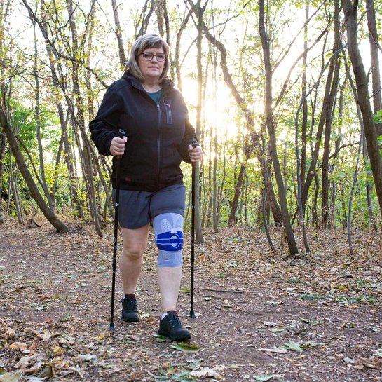 Das Bild zeigt Arthrose-Patientin Jana Eckner beim Nordic Walking im Wald. Zur Unterstützung ihres Knies trägt sie eine GenuTrain A3 Bandage von Bauerfeind.