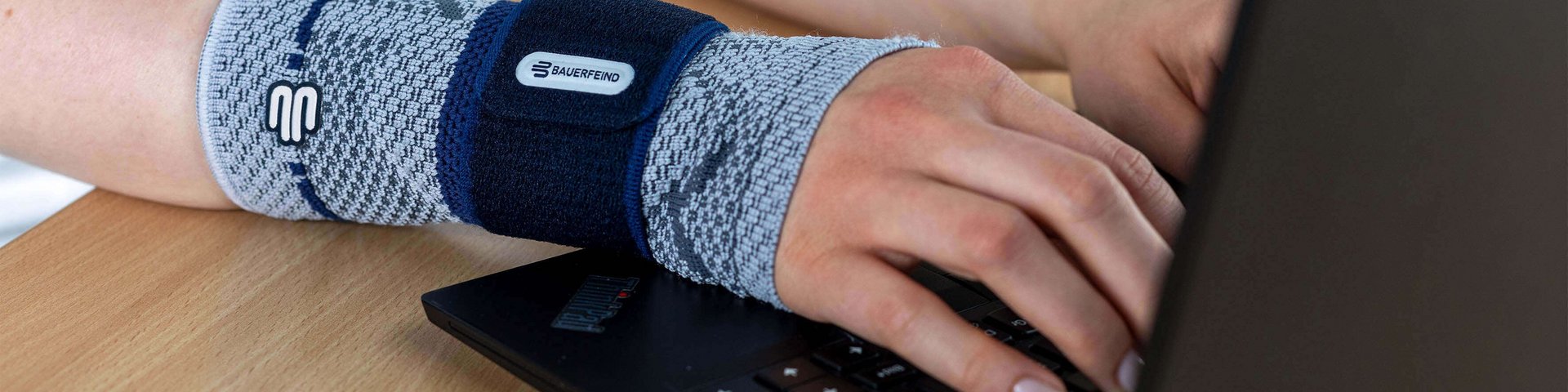 Bildausschnitt einer Frau am Laptop, die am rechten Handgelenk eine ManuTrain Bandage von Bauerfeind trägt. Diese bietet Unterstützung bei Mausarm-Beschwerden.