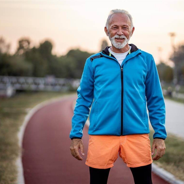 Bewegung und gesunde Ernährung sind wichtige Bestandteile der konservativen Kniearthrose-Therapie Das Bild zeigt einen älteren Mann in einem Sportoutfit auf einem Sportplatz. Er bleibt in Bewegung, um gegen arthrosebedingte Schmerzen im Griff zu behalten.
