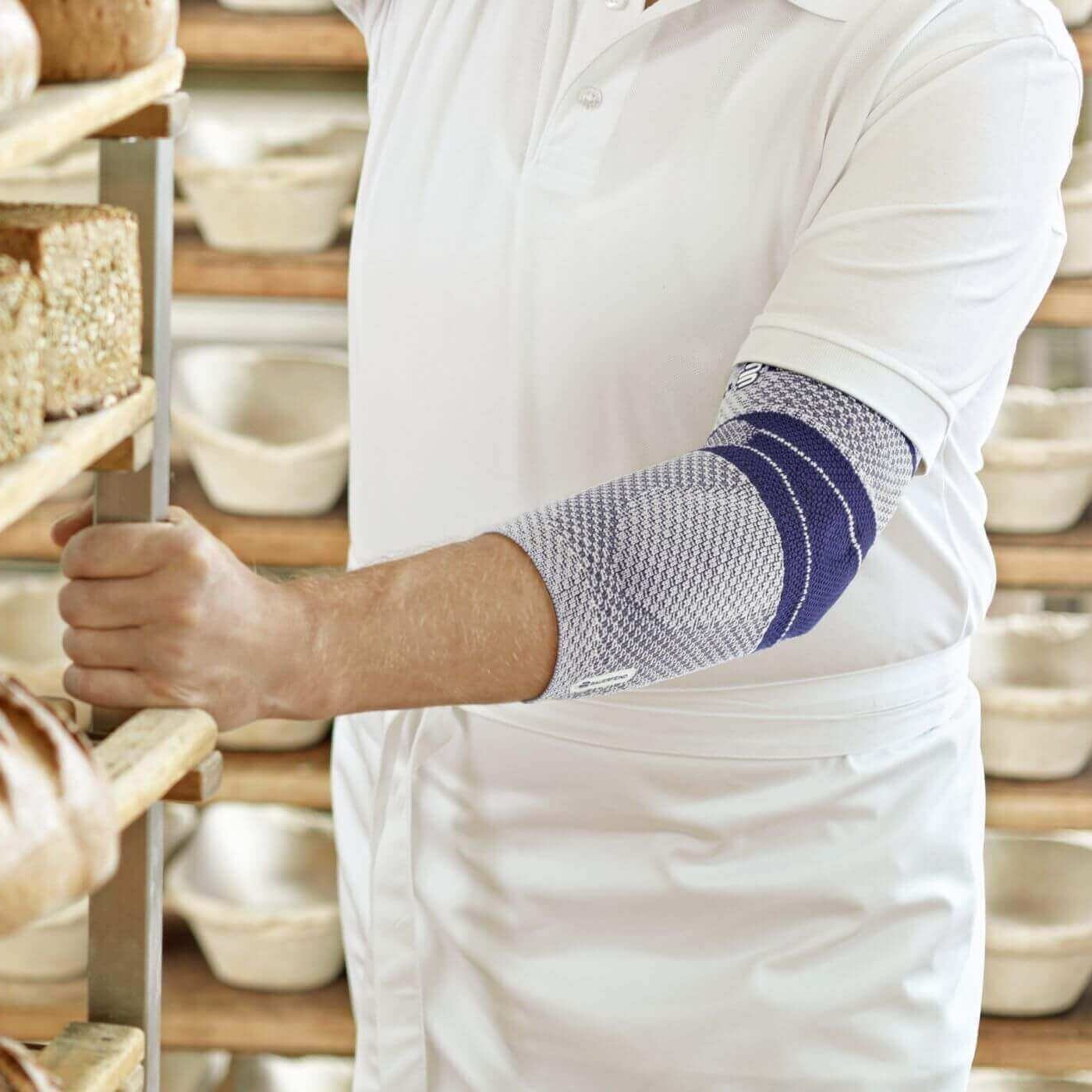 Bildausschnitt eines Bäckers in seiner Backstube. Er trägt eine EpiTrain Ellenbogenmassage von Bauerfeind am linken Arm. Die EpiTrain Bandage lindert Schmerzen im Ellenbogen und verbessert seine Beweglichkeit.