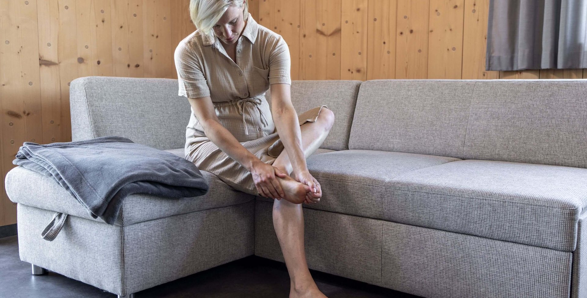 Eine schwangere Frau sitzt auf einem Sofa und massiert ihren schmerzenden Fuß, um Beschwerden zu lindern.