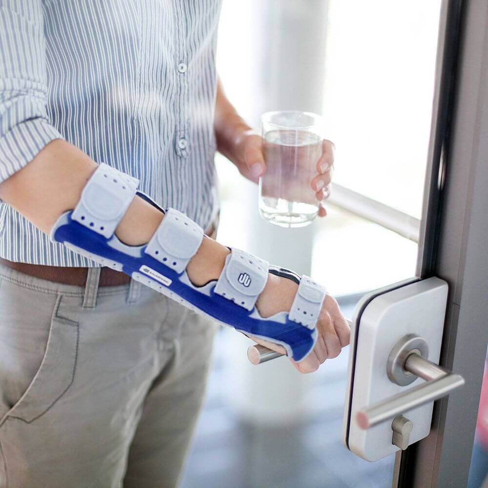 Bildausschnitt eines Mannes beim Öffnen einer Glastür. Er trägt am rechten Arm eine ManuLoc Long, eine stabilisierende Handgelenksorthese, welche unter anderem bei einem Karpaltunnelsyndrom angewendet wird.