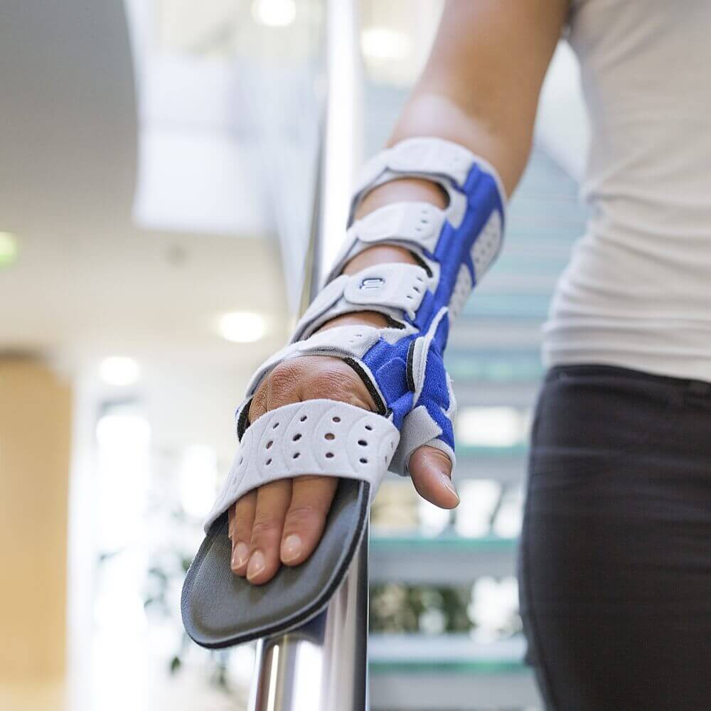 Bildausschnitt einer Frau, die eine Treppe hinab geht. An der rechten Hand trägt sie eine ManuLoc Long Plus, eine ruhigstellende Handorthese von Bauerfeind.