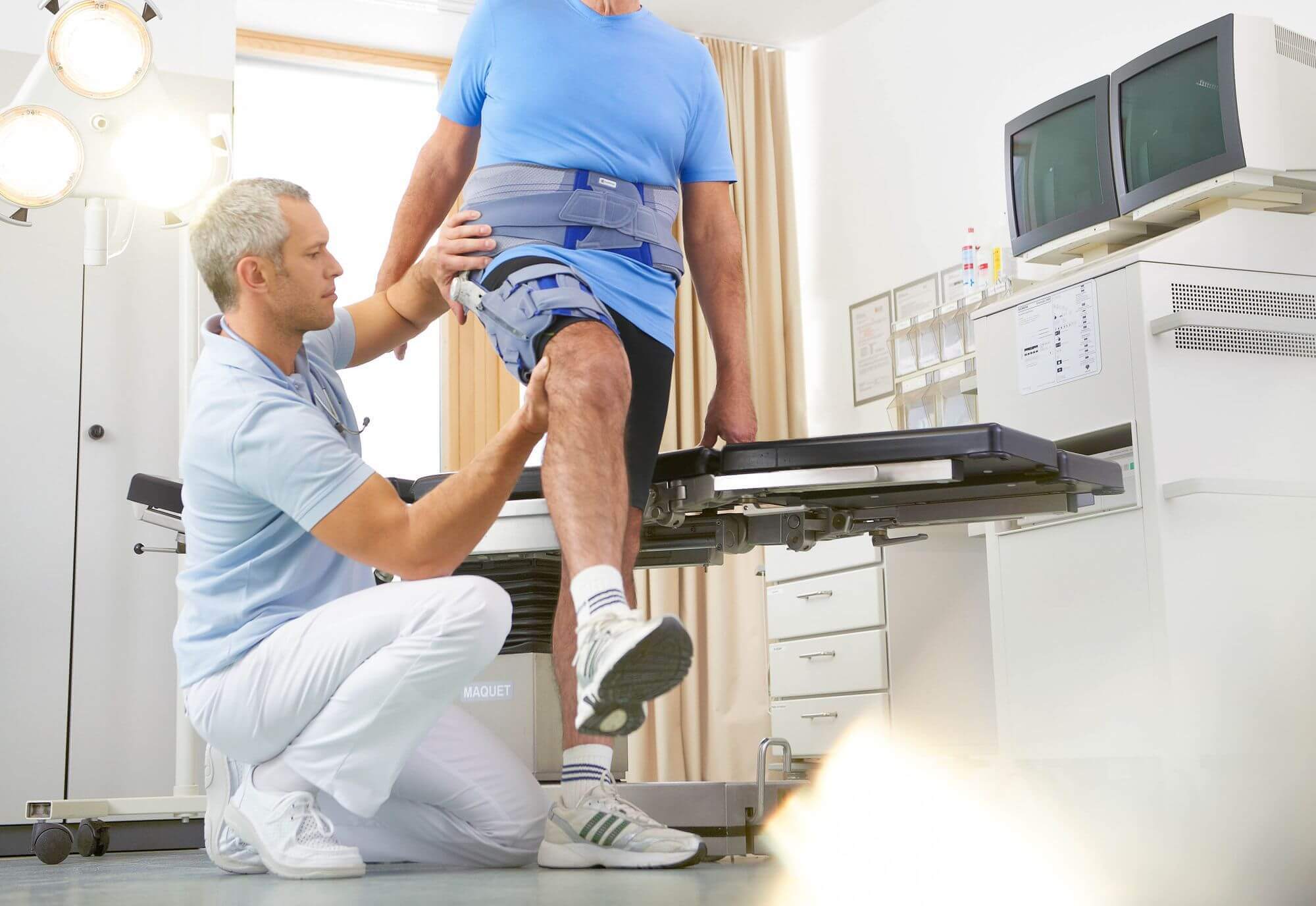 Das Bild zeigt einen Patienten mit einem Arzt im Behandlungszimmer. Der Arzt legt dem Patienten eine SofTec Coxa, eine stabilisierende Hüftorthese zur sicheren Gelenkführung von Bauerfeind, an.
